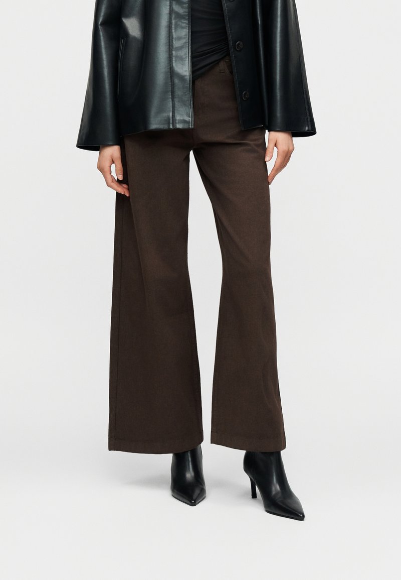 Καφέ φαρδιά παντελόνια από βαμβακερό μείγμα ύφασμα, με λεία υφή και καθαρό τελείωμα. Συνδυασμένα με μαύρα ψηλοτάκουνα παπούτσια με μυτερή μύτη.