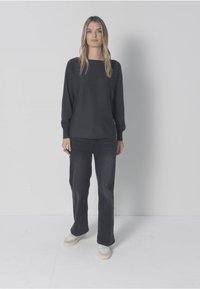 Černý top s dlouhým rukávem, volný střih, doplněný tmavými džíny. Obuv má světlou podrážku a detaily s tkaničkami. Jednoduchý a ležérní styl.