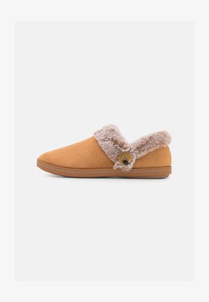 Tan suède pantoffel met een zachte, beige faux fur kraag en knoopdetail. Heeft een platte zool en gestructureerde stiksels langs de rand.