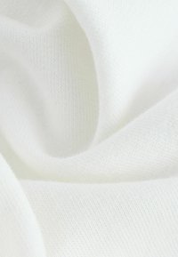 Valkoinen neulottu kangas, jossa on pehmeä, sileä pinta, hienovarainen jousto ja tasaiset, hienot silmukat kauttaaltaan.