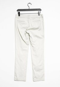 Pantalon droit beige avec poches arrière, texture lisse et taille. Suspendu sur un cintre en plastique noir sur fond blanc.