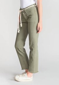 Pantalon en coton vert avec un ourlet brut, poches avant et un cordon de serrage en corde blanche. Associé à des baskets blanches.