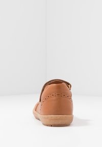 Zapato de cuero marrón con acentos perforados, un acabado suave y texturizado, y una suela de goma. Presenta un diseño sin cordones y una forma redondeada.