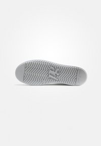 Semelle d'une chaussure, en caoutchouc blanc, présentant un motif en chevrons et un logo au centre. Bords lisses avec un bout arrondi.