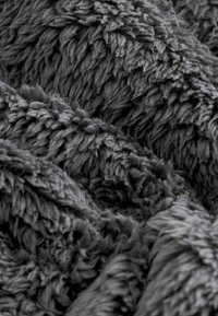 Mäkká prikrývka v tmavosivej látke s jemnou, plyšovou textúrou, ktorá má dlhý, chlpatý vlas a nepravidelný vzor po celej ploche.
