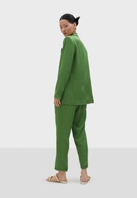 Traje verde con estampado que incluye una chaqueta ajustada y pantalones de corte relajado, hecho de una tela texturizada, combinado con sandalias de tiras.