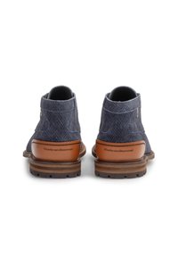 Un par de botines de tela azul marino con paneles de cuero marrón en el tacón y suelas de goma texturizada, vistos desde atrás.