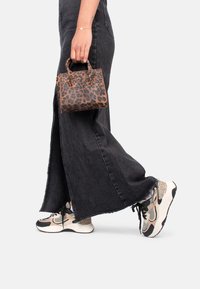 Tasche im Leopardenmuster mit doppelten Griffen, gehalten von einer Person in einem schwarzen Jeansrock und gemusterten Sneakers mit einer dicken Sohle.