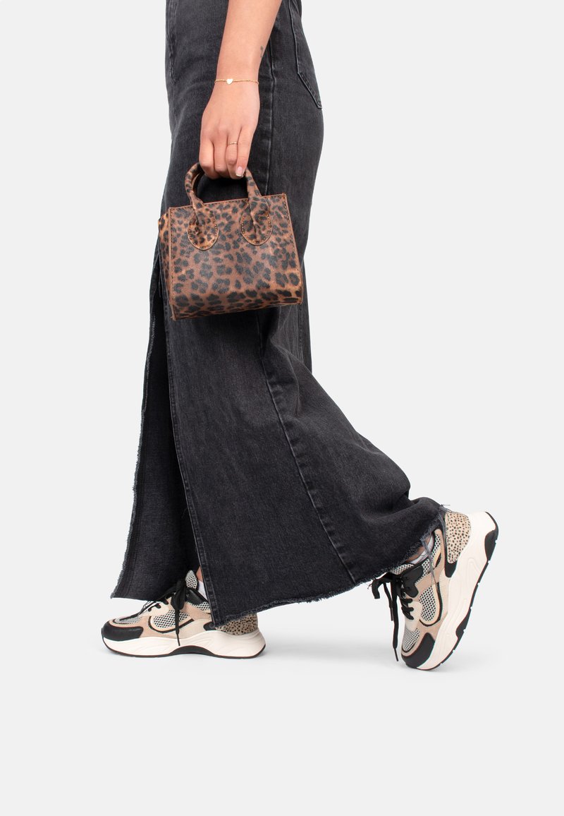 Tasche im Leopardenmuster mit doppelten Griffen, gehalten von einer Person in einem schwarzen Jeansrock und gemusterten Sneakers mit einer dicken Sohle.