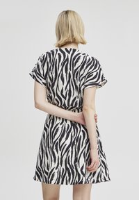 Kurzes Kleid mit einem schwarz-weiß gestreiften Zebra-Muster, aus leichtem Stoff gefertigt, mit taillierter Passform und ausgestellt Rock.