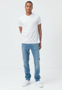 T-shirt bianco a maniche corte abbinato a jeans di denim azzurri. I jeans presentano due tasche anteriori e una texture morbida e liscia.