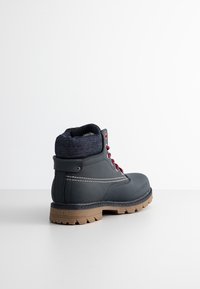 Bottine gris foncé avec lacets rouges, col en denim rembourré, couture blanche et semelle robuste beige avec la marque Levi's sur le talon.