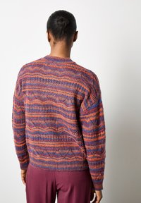 Knitted sweater featuring a multicolored pattern with wavy lines in orange, purple, and blue. Ribbed cuffs and hem. Oversized fit.