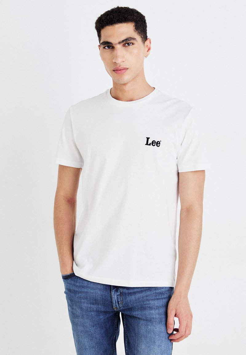 Fehér pamut póló, bal mellen fekete hímzett "Lee" logóval, kerek nyakkivágással és rövid ujjú, kék denim farmernadrággal párosítva.