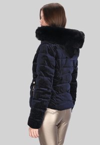 Párnázott tengerészkék dzseki műszőrme kapucnival, texturált anyagból, oldalsó cipzárakkal és testhez simuló szabással, fényes arany metál nadrággal párosítva.