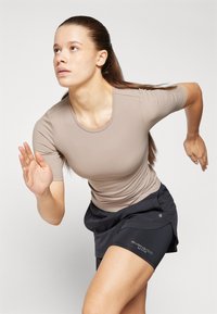 Svijetlo smeša sportska majica s kratkim rukavima u kombinaciji s crnim trkaćim kratkim hlačama. Ima fleksibilan kroj i glatku teksturu.
