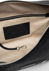 Zwarte leren handtas interieur met een beige voering, met een ritsvak, een zwart etiket en een zilveren clip om items veilig te stellen.