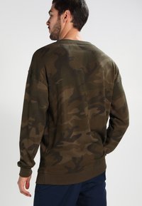 Felpa a maniche lunghe verde oliva con motivo mimetico, scollo rotondo e polsini e orlo a costine. Tessuto morbido con una vestibilità comoda.