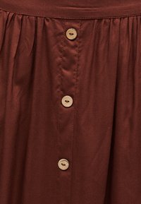 Καφέ ύφασμα με τρία μπεζ κουμπιά σε κάθετη σειρά και μάζεμα ραφής κοντά στην επάνω άκρη.