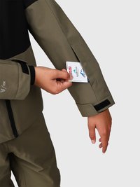 Chaqueta de esquí verde oliva con sección superior negra. Presenta un bolsillo con cremallera en la manga, donde se puede ver una tarjeta parcialmente insertada.
