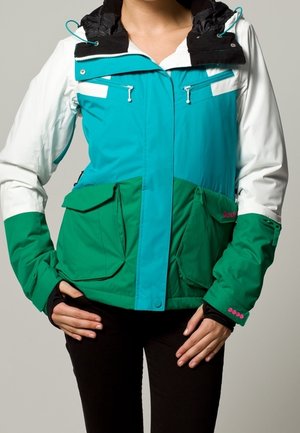 Giacca multicolore con cappuccio nero, corpo turchese e verde, due grandi tasche frontali e tasche pettorali con zip, realizzata in un materiale morbido.