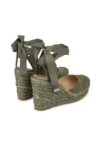 Sandali con tacco a zeppa in suede verde, con un tacco in juta intrecciata, caratterizzati da nastri in raso alla caviglia e un design con punta aperta. Texture liscia e finitura morbida.