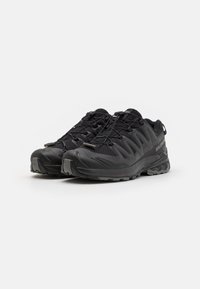 Black athletic shoes with mesh upper, curved design, and textured rubber sole. Features elastic laces and reinforced toe cap. Lightweight construction.