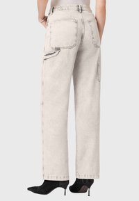 Lichtgrijze wijde jeans met twee achterzakken, een zijzak en contrasterende stiksels, gecombineerd met zwarte, getextureerde hakken.