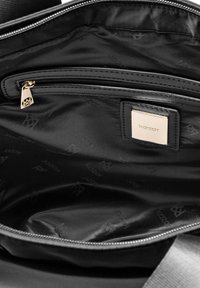 Svart tygväska med insida som har en dragkedjeficka, guld dragkedjeöppnare och en guldplakett märkta "kazar" på den släta foder.