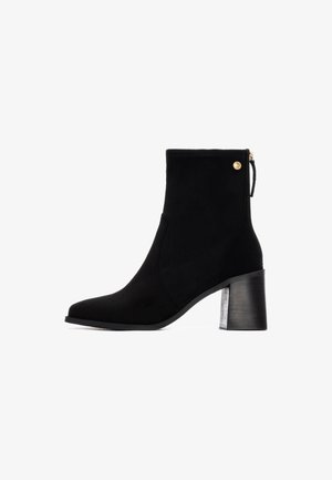 Botín de ante negro hasta el tobillo con puntera cuadrada, cierre de cremallera y tacón en bloque texturizado. Presenta un acento dorado en el costado.