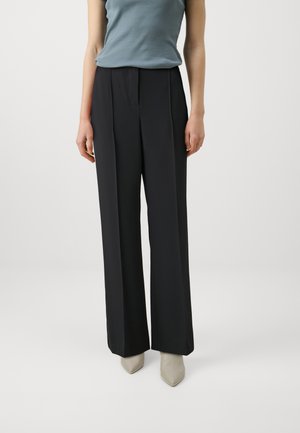 Black, wide-leg trousers with a flat front design and pleats. Worn with a light blue top and beige pointed-toe shoes on a neutral background.