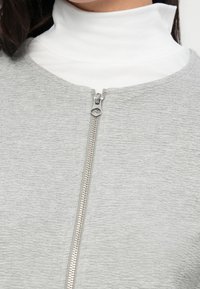 Γκρι ρούχο με φερμουάρ, από υφή υφάσματος, με ασημένιο φερμουάρ και λευκό ψηλό γιακά από μέσα.
