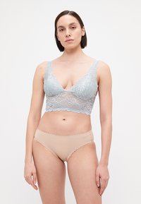 Gaiši zila mežģīņu bralete ar viļņotām malām, ar V veida dekoltē. Kombinēta ar nude krāsas bezšuvju bikini apakšdaļām. Gluda tekstūra visā virsmā.