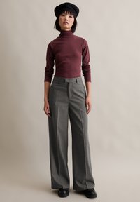 Burgundowy sweter z kołnierzem typu golf w połączeniu z szarymi spodniami w szerokie paski. Uzupełnieniem stroju jest czarna beretka i masywne czarne buty.