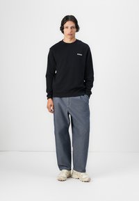 Sort sweater med rund hals, prydet med et lille logo. Sammen med afslappede, lyseblå jeans og sneakers i kremfarve.