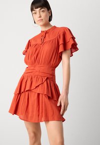 Rochie scurtă portocalie cu mâneci volanate și fustă în straturi. Material texturat cu talie ajustată și noduri decorative la decolteu.