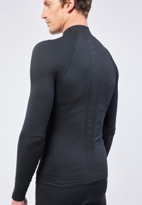 Schwarzes, figurbetontes Langarm-Thermoshirt mit strukturierten Mustern an den Schultern und in der Mitte, Rundhalsausschnitt und elastischen Bündchen. Zusätzliche Markenkennzeichnung auf der Rückseite.
