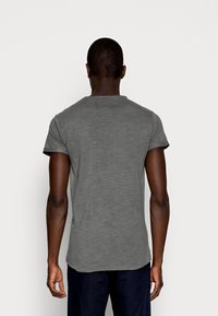 Grå T-shirt med korte ærmer og rund hals, glat tekstur og afslappet pasform, set bagfra. Kantene er lidt buede.