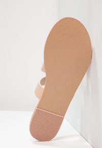 Sandal in rosa chiaro, tipo slip-on, con tomaia testurizzata, suola piatta con linee di grip e logo in rilievo. Design minimalista con punta aperta.