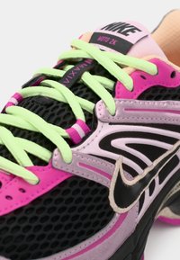 Sapatos Nike com um cabedal em malha nas cores preto, rosa e púrpura, com atacadores verdes-limão e um detalhe de swoosh preto. Superfícies texturizadas são visíveis.