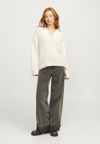 Maglione bianco in morbido knit con scollatura a V e spalle cadenti, abbinato a jeans grigi scuri a gamba larga e stivali neri con suola spessa.