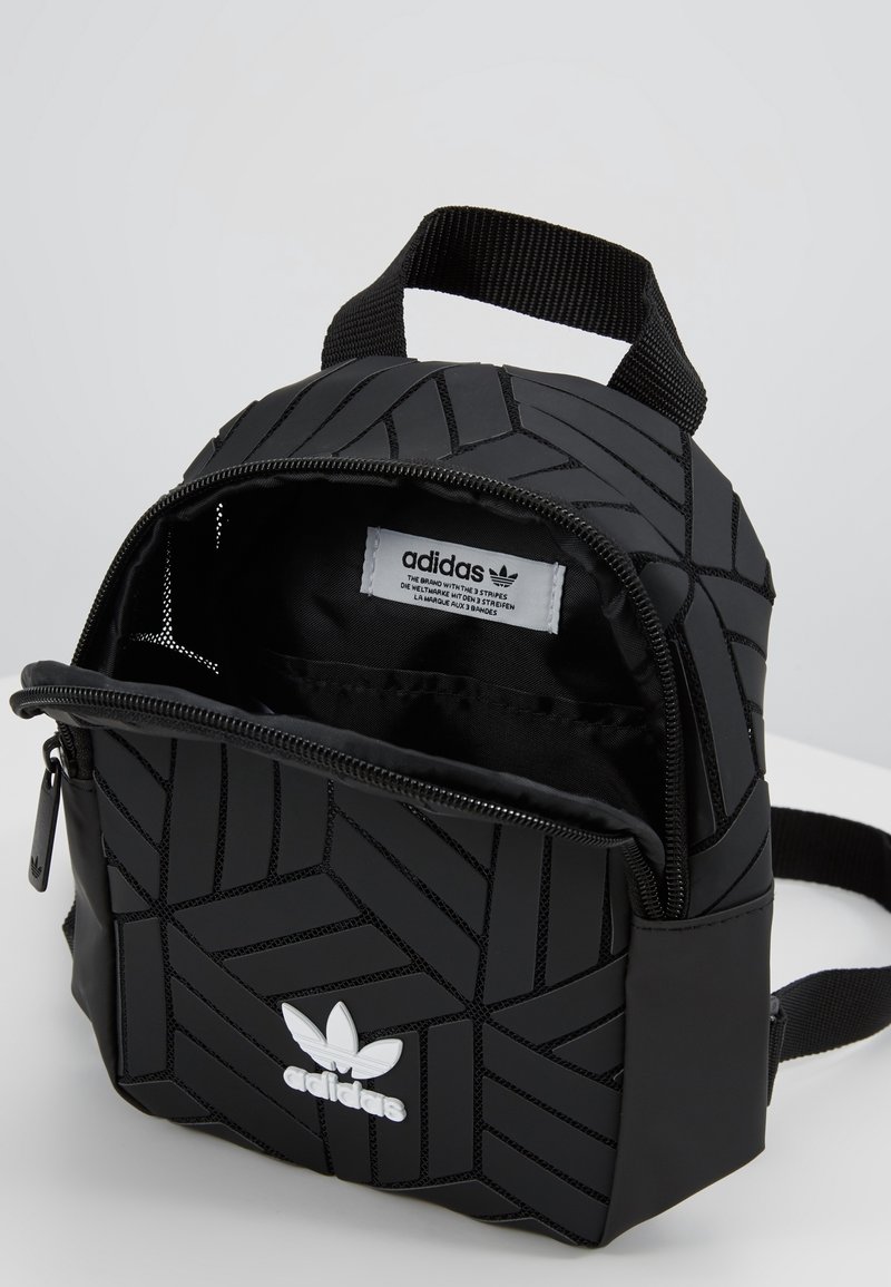 Svart Adidas mini-ryggsäck med geometriskt mönster, dragkedja, vitt logo, texturerat material och justerbar rem.