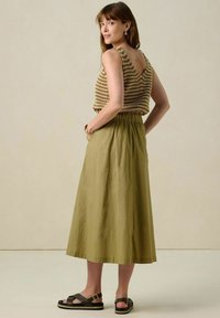 Débardeur en tricot rayé avec un dos en V, associé à une jupe verte olive arrivant aux genoux et des sandales noires avec un détail de boucle.