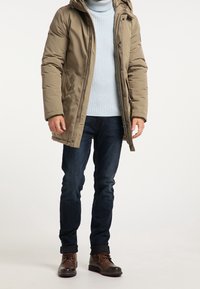 Béžová péřová bunda s kapucí, zapínáním na zip a knoflíky, nošená přes světle modrý žebrovaný svetr, v kombinaci s tmavými džínami a hnědými šněrovacími botami.