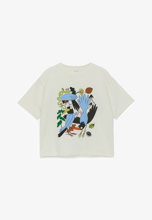 T-shirt blanc à manches courtes avec un graphique coloré sur le devant représentant des oiseaux cartoon, des feuilles, une fleur, une pomme de pin, un coléoptère et un bouchon de bouteille de soda.