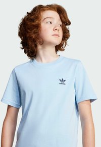 Hellblaues Baumwoll-T-Shirt mit rundem Ausschnitt, kurzen Ärmeln und einem dunkelblauen Adidas-Logo auf der linken Brust gedruckt. Glatte Textur.