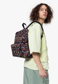 Mochila de tela negra cubierta de coloridos logotipos y personajes de cómic. Cuenta con correas acolchadas y un bolsillo delantero.