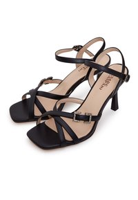 Sandales à talons hauts noires à lanières avec un bout ouvert, dotées d'un accent de boucle carrée et d'une texture en cuir lisse sur une semelle intérieure beige.