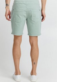 Pantaloni scurți verde deschis din bumbac, cu talie elastică, două buzunare în spate și tiv rulant. Textură netedă cu detalii minimale.