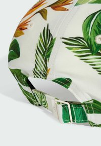 Gorra ajustable con un fondo blanco que presenta vibrantes patrones de hojas tropicales en verde y naranja. Tejido suave y cierre de hebilla de plástico.